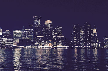 The Boston Skyline lit up at night with city lights from the perspective of the water