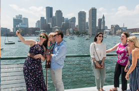 Family taking a selfie on the bow of a classic yacht with the Boston Skyline in the Background