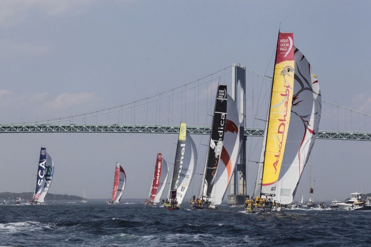 Multiple sailboats racing in a harbor for the Volvo Race Series with a bridge in the background
