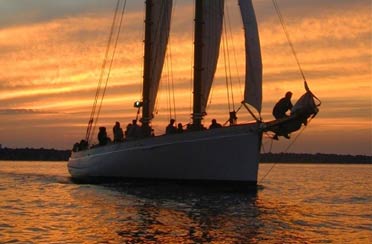 Schooner Adirondack II sailing at sunset with a golden sky in the background of Boston Harbor