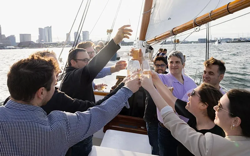 a group of people cheering with glasses of champagne, aboard a sailboat in Boston