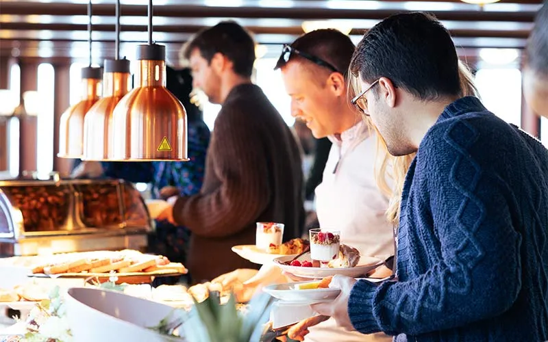 a group of people in a buffet line, grabbing various food options