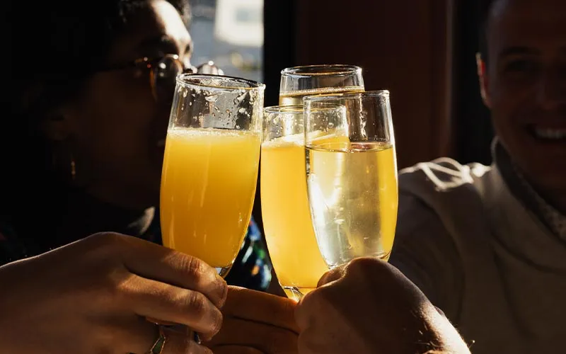 closeup of a group of friends cheering with glasses of mimosas