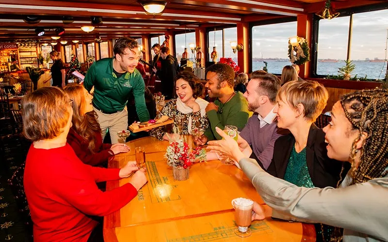 a group of people sitting at a table with drinks, being served Hors d'oeuvres by a waiter