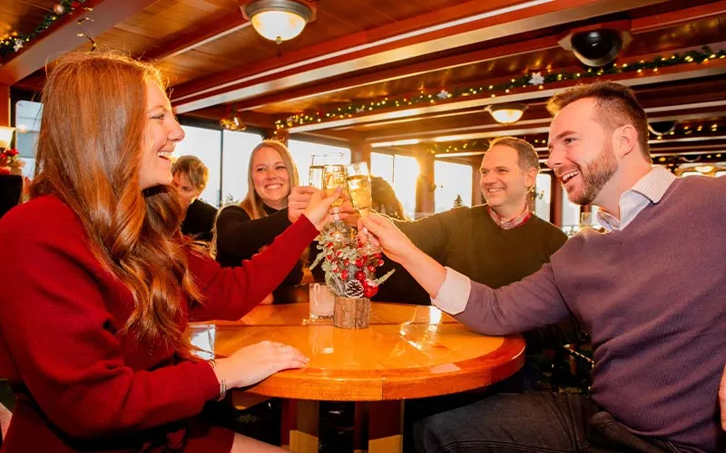 two men and two women, cheering with drinks, while sitting at a table inside of the motor yacht northern lights