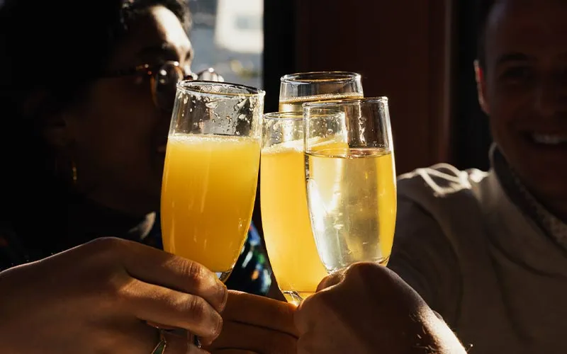 a group of people cheersing glasses of mimosa