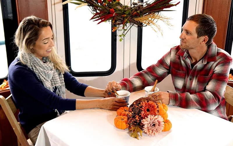 a man and a woman, holding hands, while chatting at a fall decorated table aboard a yacht