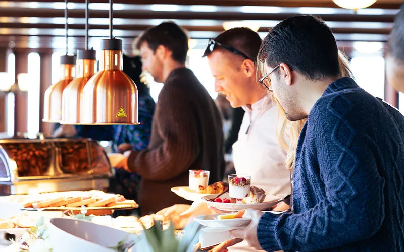a group of people in a buffet line, grabbing various food options