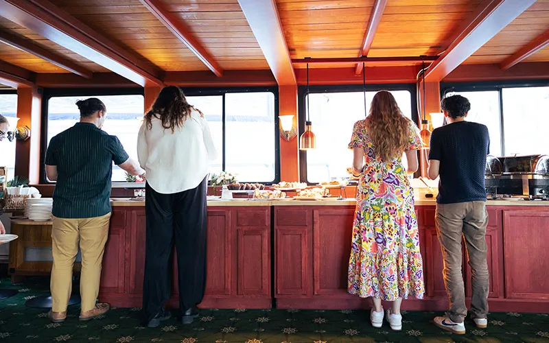 Boston_Fall-Foliage-Luncheon-Slider-2 a group of people in front of a table, grabbing hor d'oeuvres