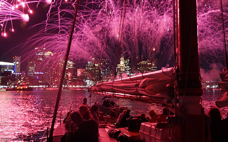 groups of people on a sailboat, watching fireworks being shot over the Boston harbor