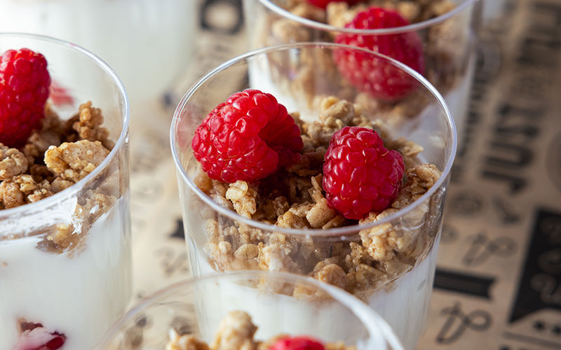 close up view of yogurt cups, with raspberries and granola on top