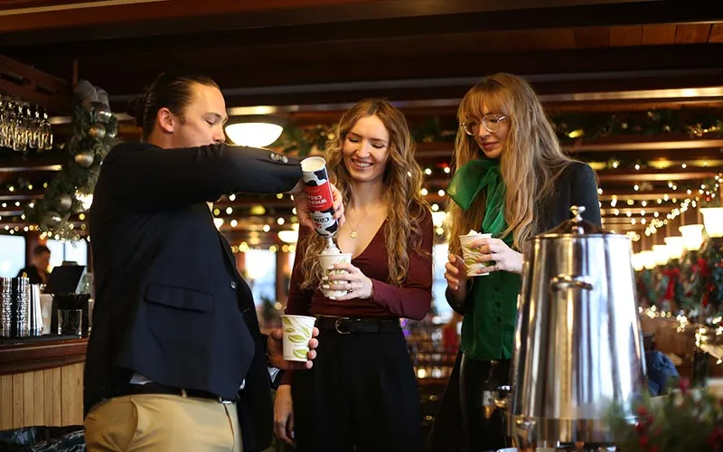 two women getting whipped cream poured on top of their cups by a man