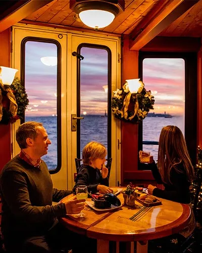 a family of three, looking out over the water, inside of a holiday decorated motor yacht