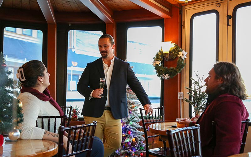 two men and a woman, all nicely dressed socializing inside of a motor yacht that is holiday decorated