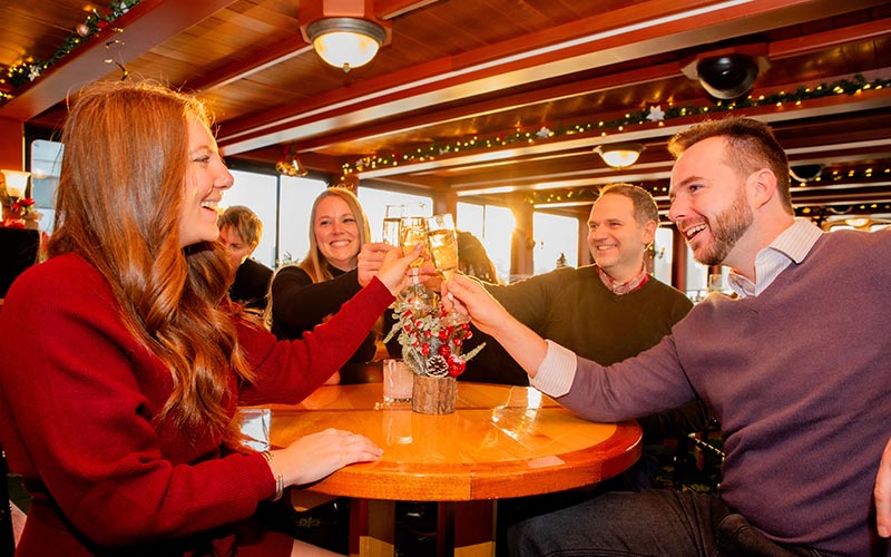 two men and two women, cheering with drinks, while sitting at a table inside of the motor yacht northern lights