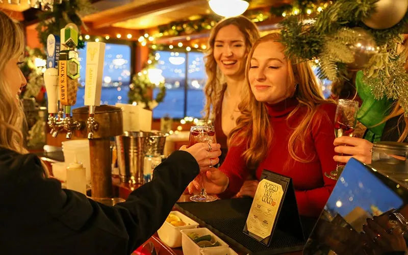 two women purchasing drinks at a bar, surrounded by holiday decor inside of a motor yacht