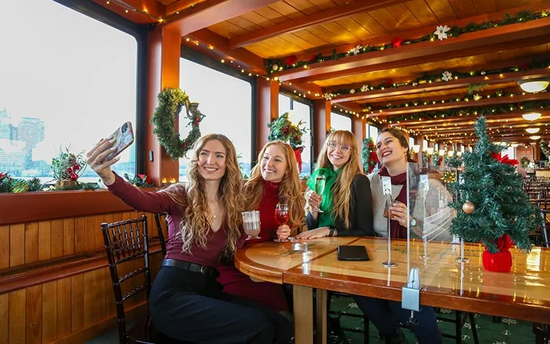 a group of three women taking a selfie together, aboard a holiday decorated motor yacht