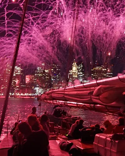groups of people on a sailboat, watching fireworks being shot over the Boston harbor