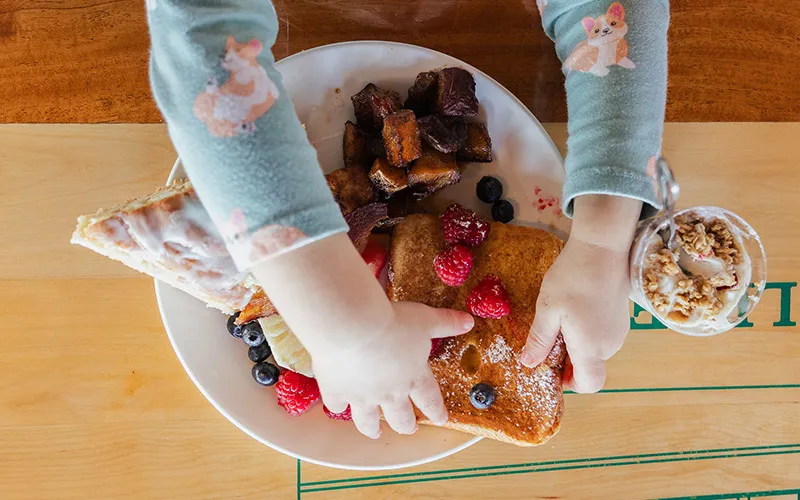 closeup of a small child reaching and grabbing french toast off a plate