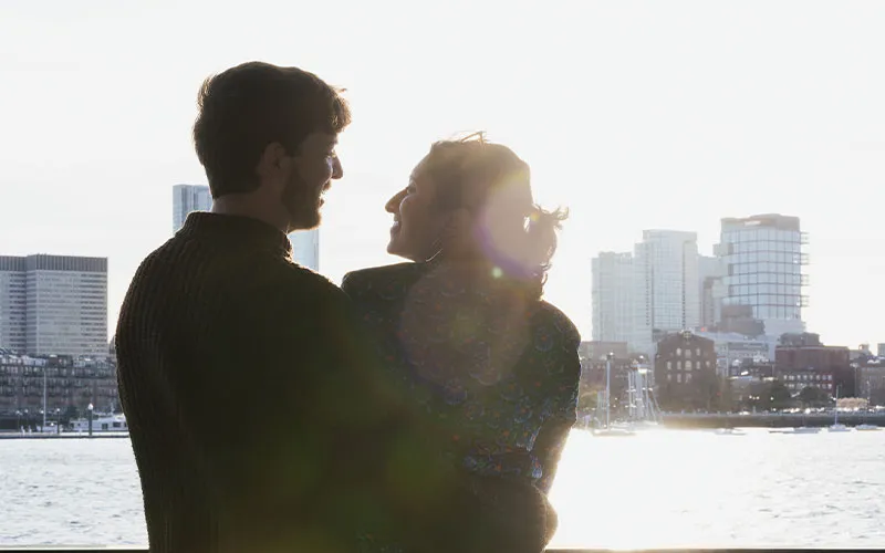 Boston_Northern-Lights-Sunset-Slider-2 a man and a woman looking at each other, aboard a yacht, with the city landscape in the distance