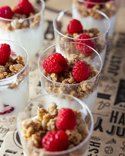 close up view of yogurt cups, with raspberries and granola on top
