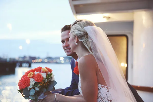 a man and a woman, looking out over the railing on a sailboat, both just recently married