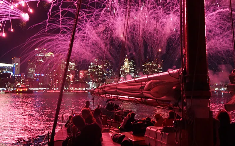 groups of people on a sailboat, watching fireworks being shot over the Boston harbor