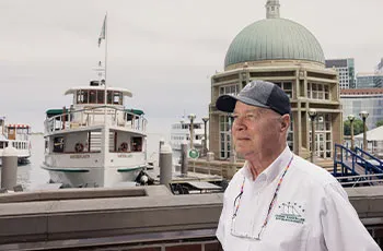 a Boston embassador, walking down past a Boston harbor with a motor yacht seen parked there