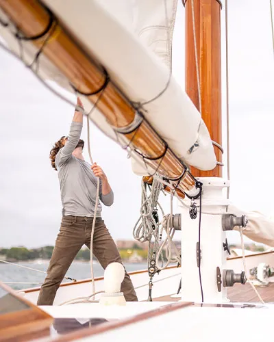 two men pulling ropes attached to sails, while aboard a sailboat