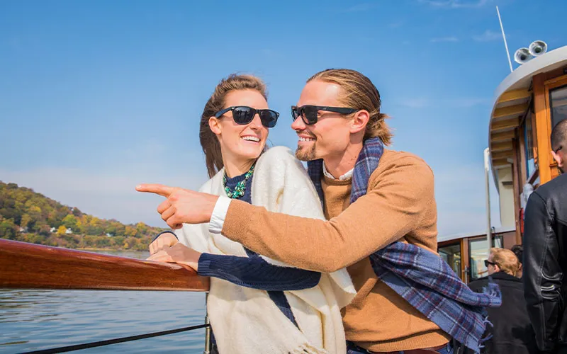 Boston_Gift-Certificates-Main a man and a woman close to each other and smiling, leaning on a railing of a motor yacht