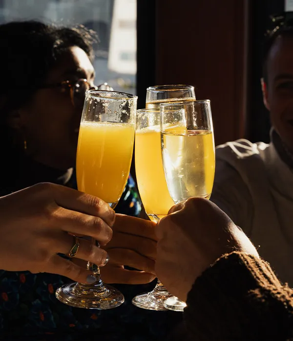closeup of a group of friends cheering with glasses of mimosas