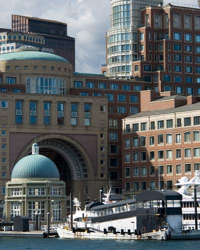 large buildings in downtown Boston, with some motor yachts seen docked at a pier