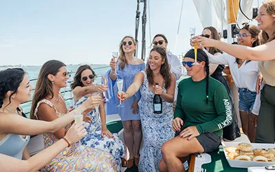 a group of women cheering with a bottle of champagne aboard a sailboat