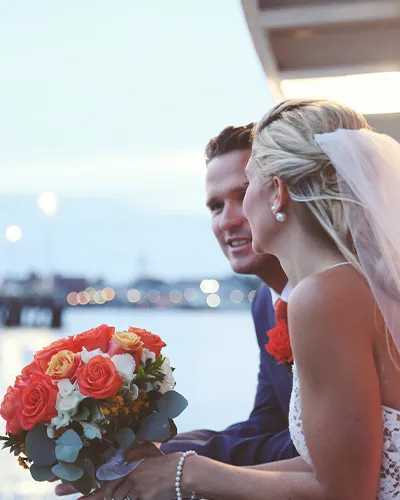 a man and a woman, looking out over the railing on a sailboat, both just recently married