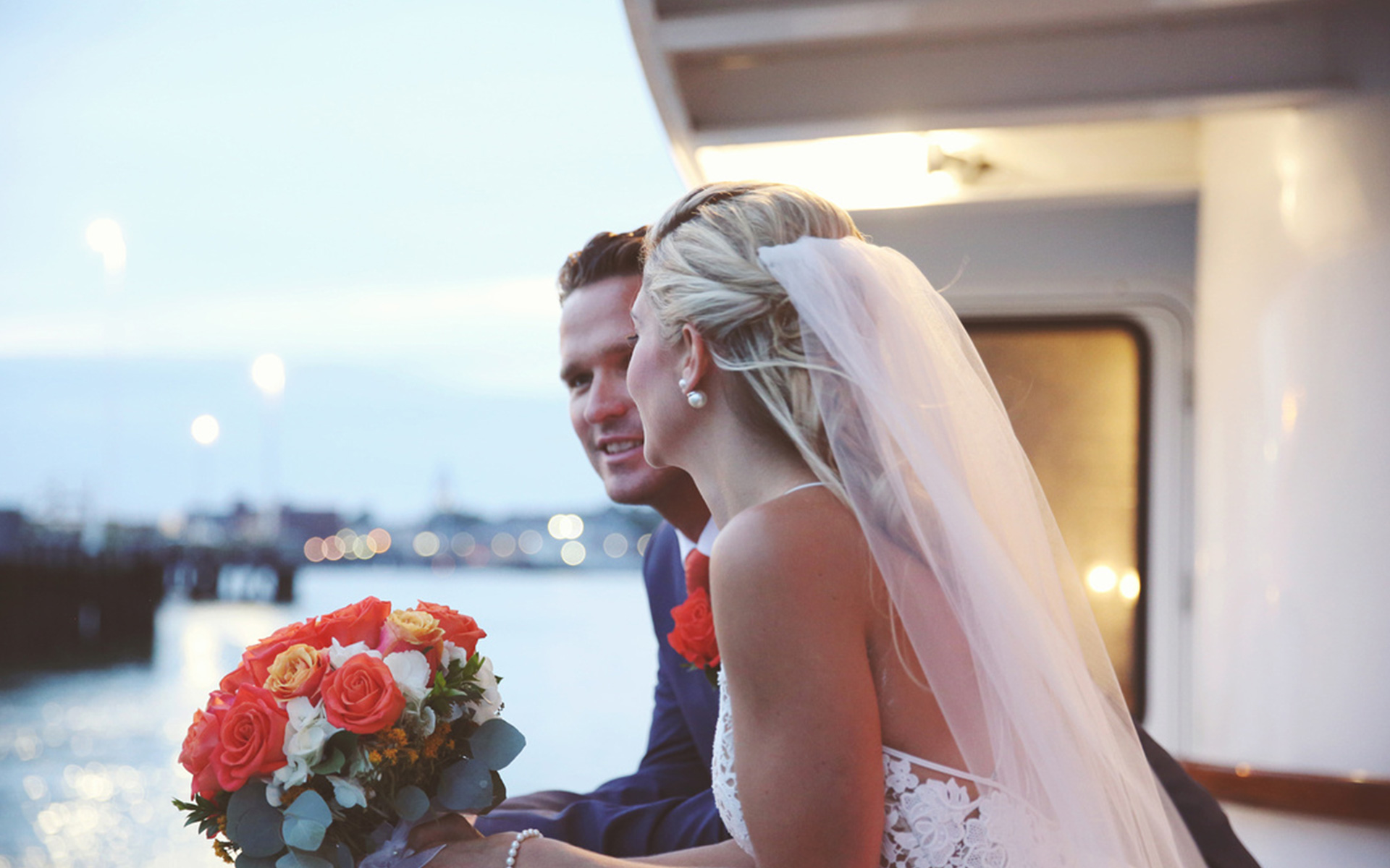 a man and a woman, looking out over the railing on a sailboat, both just recently married