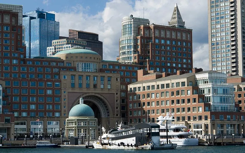 large buildings in downtown Boston, with some motor yachts seen docked at a pier