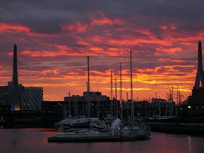 the Boston harbor with sailboats docked, and a sunset in the distance