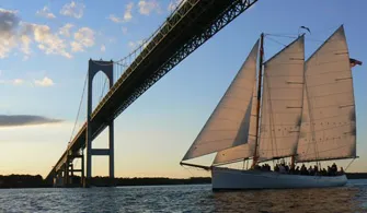 the Schooner Adirondack II sailboat cruising under a large bridge on the water