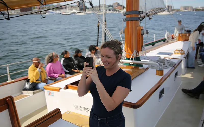 Woman taking a photo on a sail boat in Boston Harbor