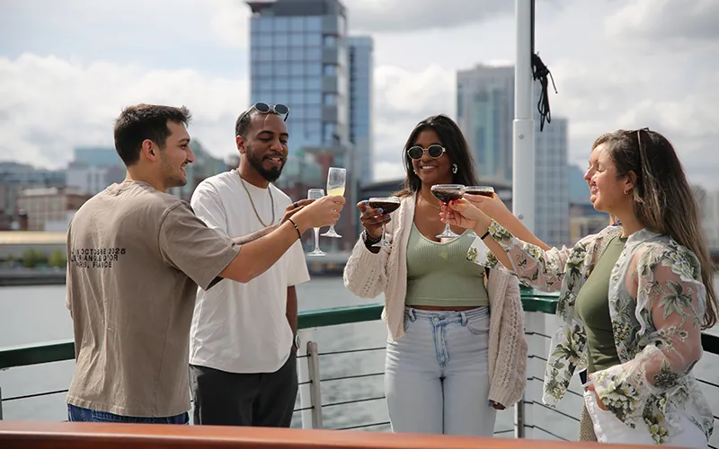 Friends on the bow of yacht Northern Lights with the Boston Skyline in the background on a sightseeing boat tour
