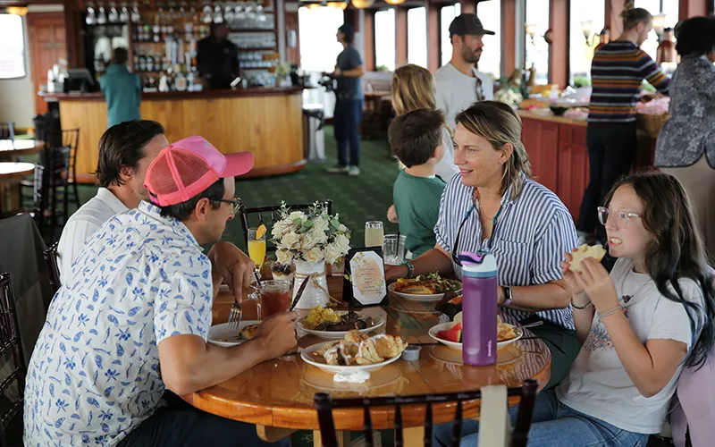 Group of friends sitting at a table in the grand salon of the yacht Northern Lights enjoying brunch