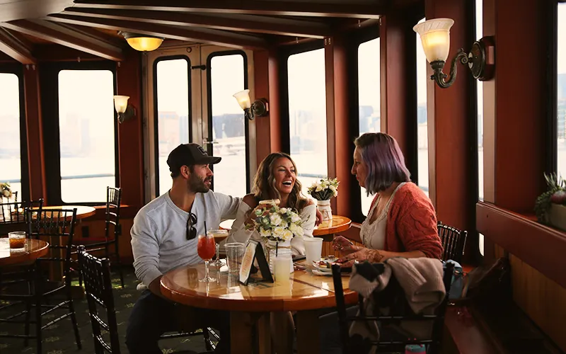 Group of friends enjoying brunch in the grand salon of the yacht Northern Lights with the Boston Skyline in the background