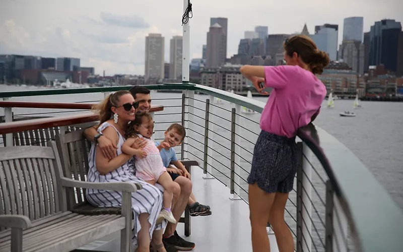 Woman taking a picture of a family on the bow of the yacht Northern Lights with the city in the background