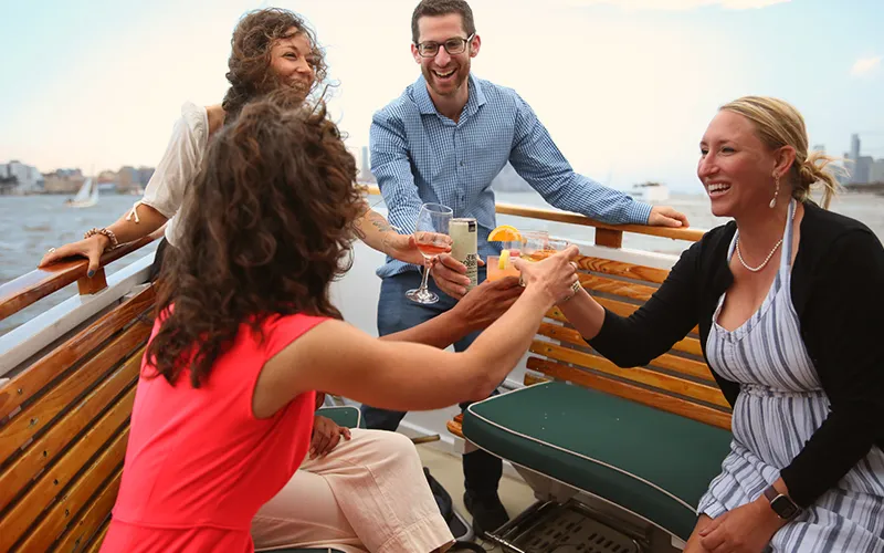 Group of friends enjoying cocktails on the bow of the yacht Patriot in Boston Harbor for a sunset cruise