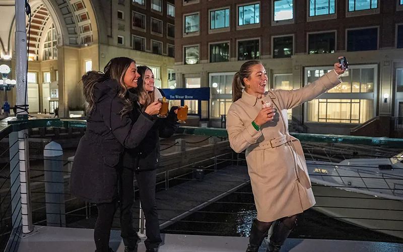 Group of friends taking a selfie on the bow of yacht Northern Lights with the Boston Harbor Hotel in the back