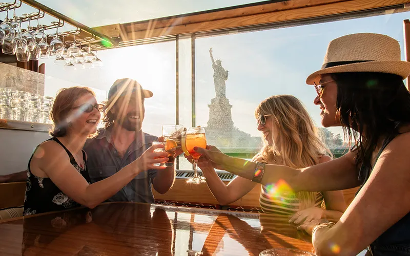 Friends enjoying cocktails on a yacht with the statue of liberty in the background